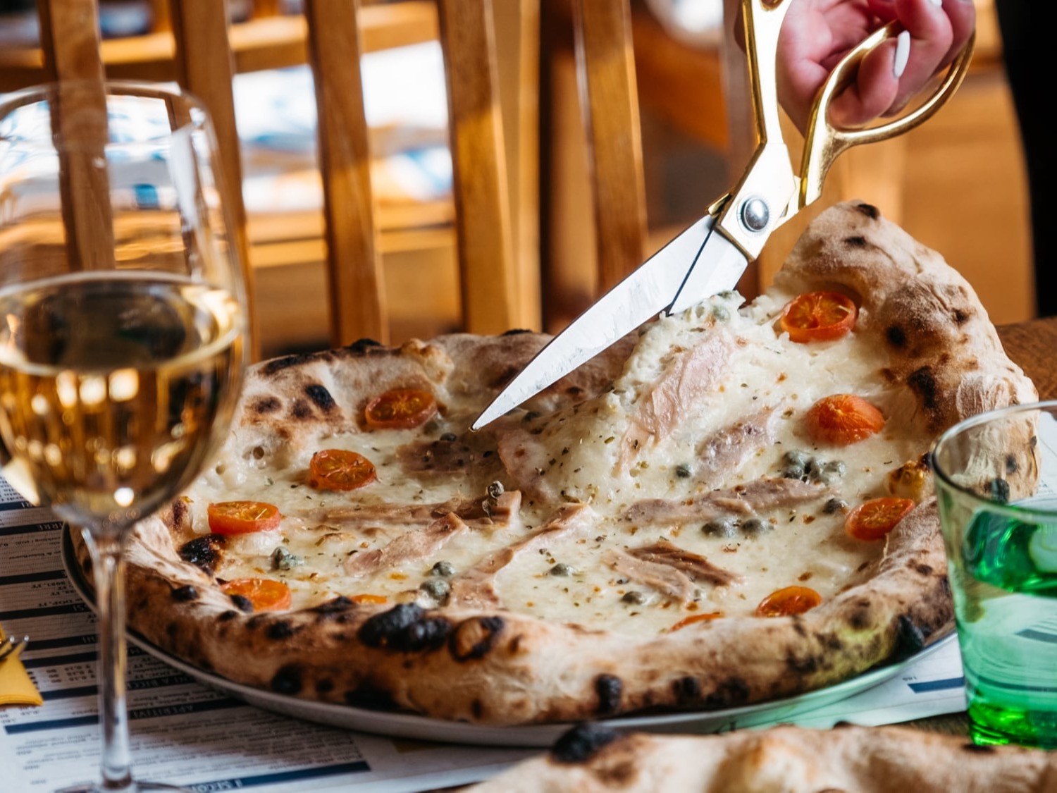 Krájení neapolské pizzy nůžkami u stolu v restauraci Papaiolo