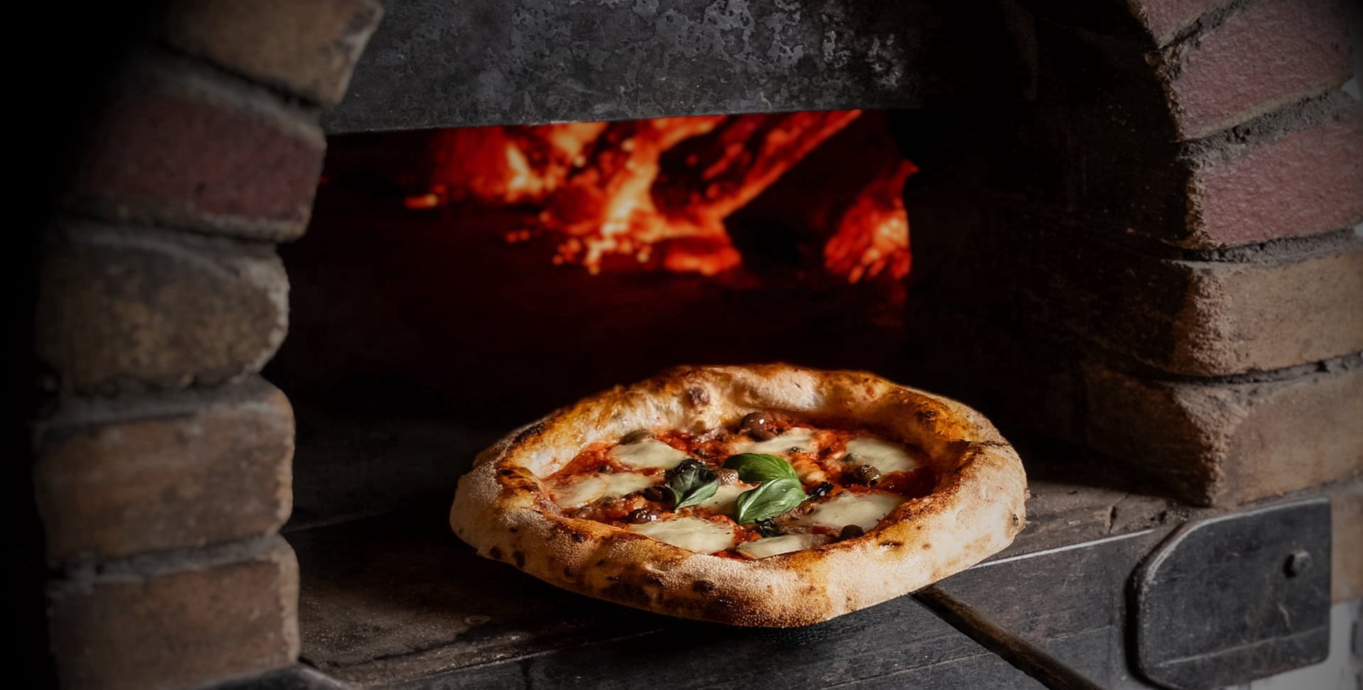Wood-fired stone oven with flames cooking fresh authentic Neapolitan pizza at Papaiolo Prague restaurant