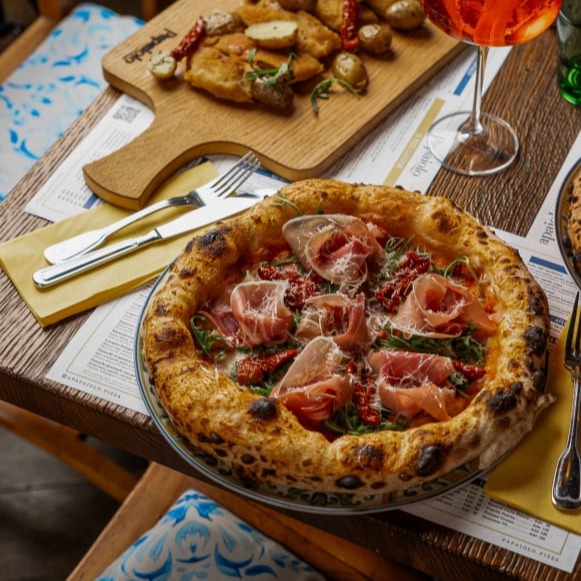Neapolská pizza s prosciuttem a rukolou na keramickém talíři