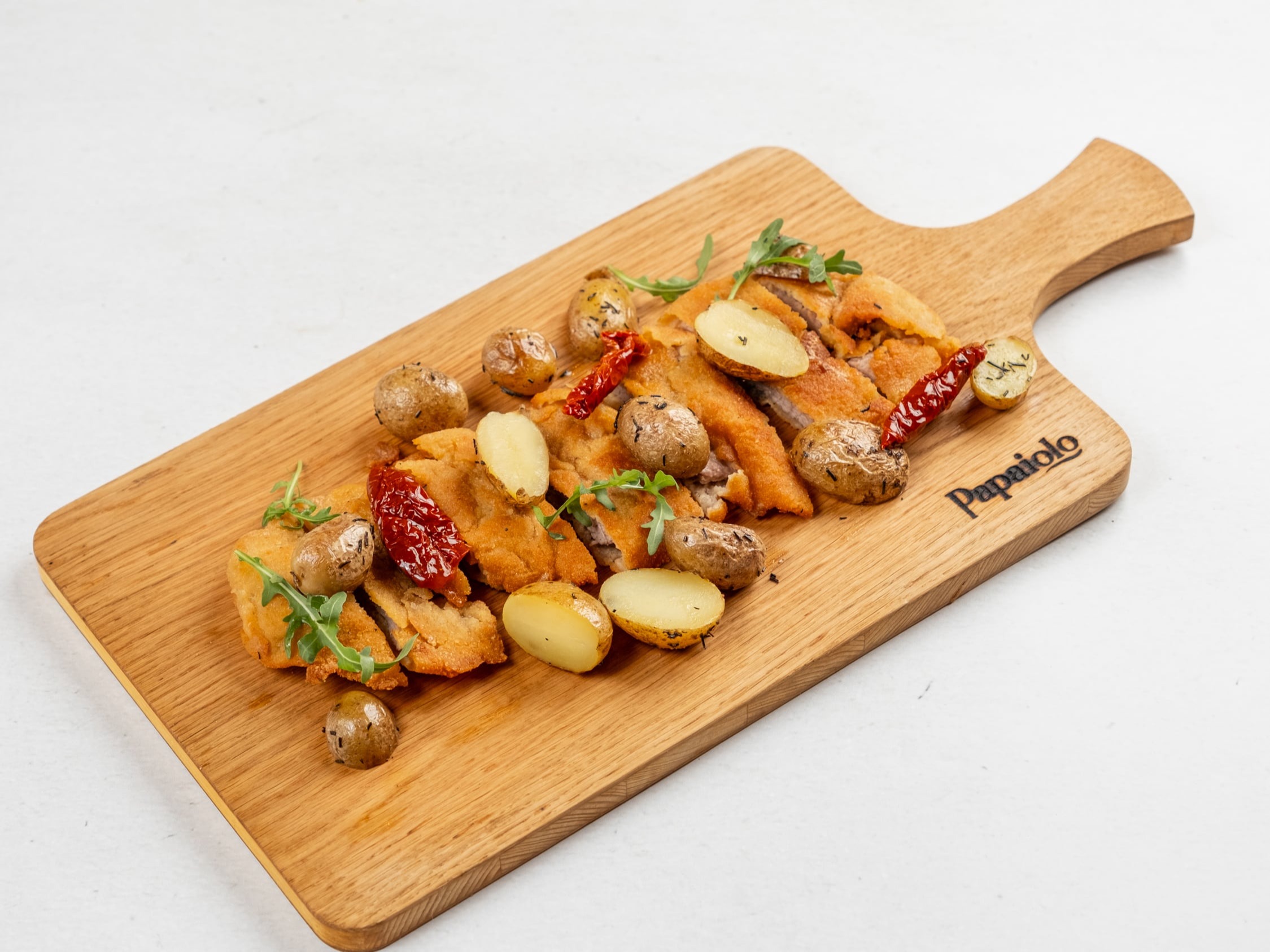 Cotoletta di vitello alla milanese con patate al forno alle erbe e pomodori secchi su tagliere di legno
