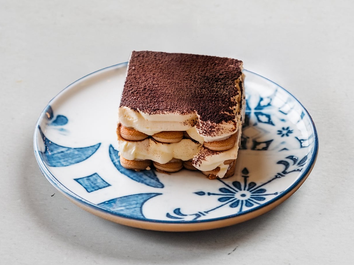 Tiramisù della casa spolverato di cacao su piattino in ceramica